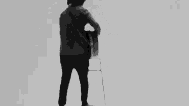 a man is playing a guitar while standing on a stool in a black and white photo .