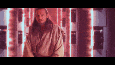 a man with long hair and a beard is standing in front of a wall with red lights behind him .