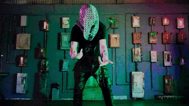 a man with a mask on his head stands in front of a wall with boxes on it