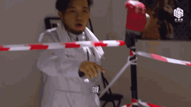 a man wearing boxing gloves stands behind a red and white tape barrier