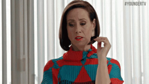 a woman in a red and blue sweater is talking on a cell phone in front of a window .