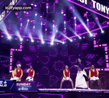 a group of dancers are dancing on a stage in front of a purple background .
