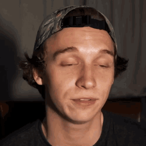 a young man wearing a baseball cap is making a funny face with his eyes closed