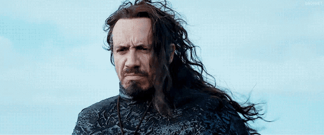 a man with long hair and a beard is standing in the wind