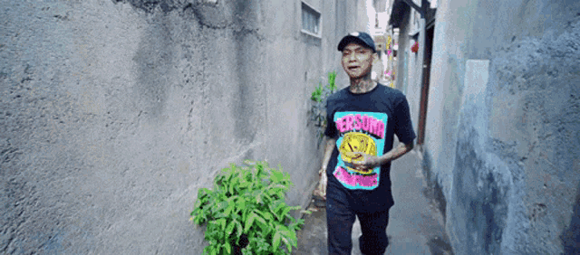 a man walking down a narrow alleyway wearing a t-shirt that says ' trash ' on it