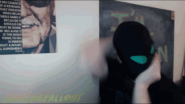 a man wearing a mask stands in front of a poster that says ' i am the fallout '