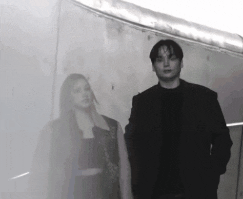 a man and a woman are standing next to each other in front of a white wall