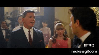 a man in a tuxedo and tie is talking to a woman in a red dress .