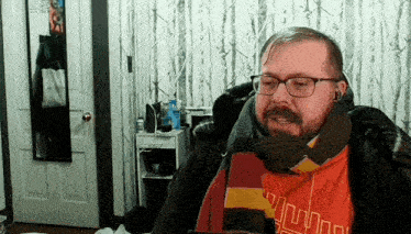 a man with glasses and a scarf around his neck is wearing an orange shirt that says ' nm ' on it