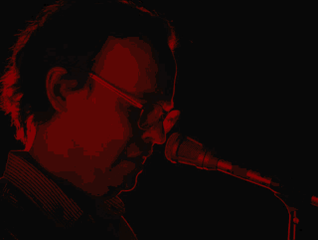 a man with glasses singing into a microphone in a dark room