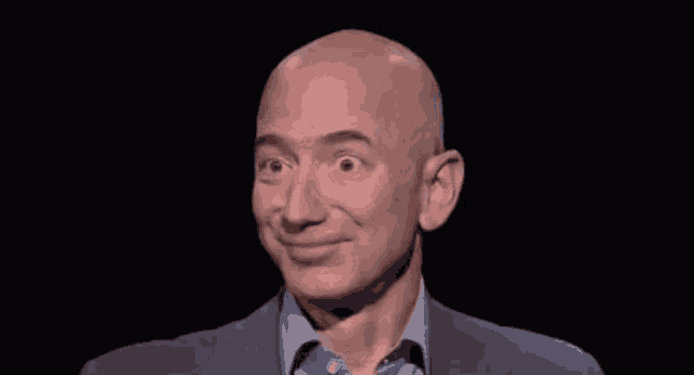a bald man in a suit and blue shirt is smiling against a black background .