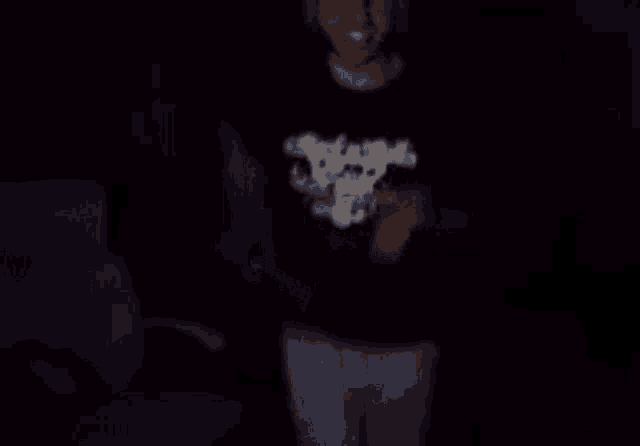 a man is dancing in a dark room wearing a black shirt with a skull on it .