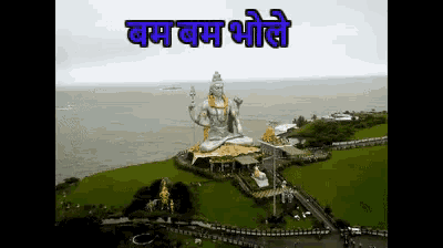 a large statue of shiva sits on top of a grassy hill overlooking the ocean