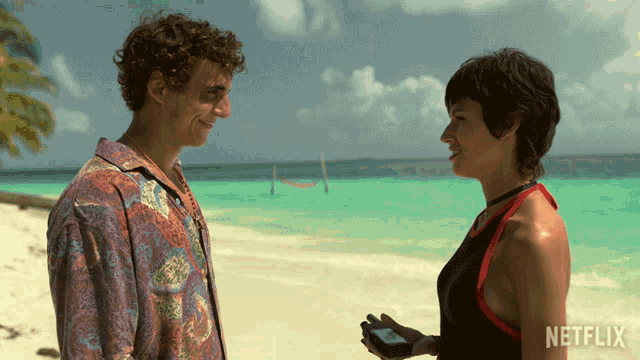 a man and a woman standing on a beach with netflix written on the bottom