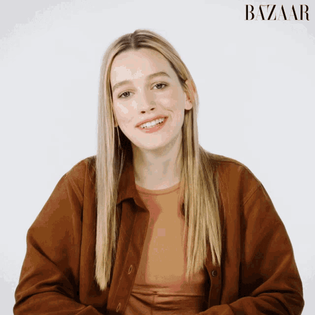 a woman in a brown jacket is smiling in front of a harper 's bazaar logo