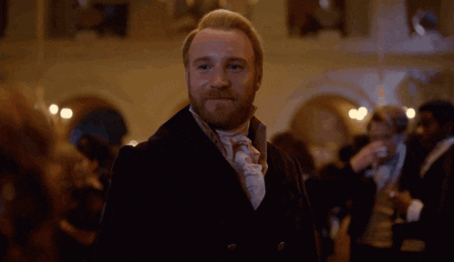 a man with a beard and tie is standing in a crowded room