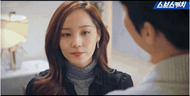 a man and a woman are looking at each other and the woman is wearing a turtleneck and earrings .
