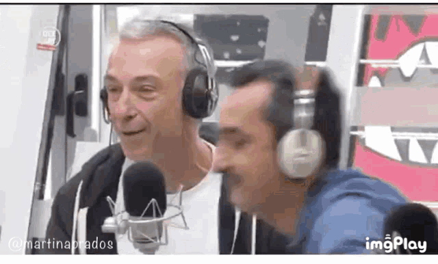 two men wearing headphones are sitting in front of microphones and smiling .