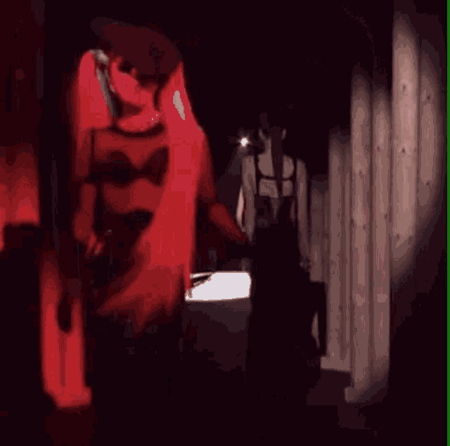 a woman in a black dress is walking down a dark hallway with a red light behind her