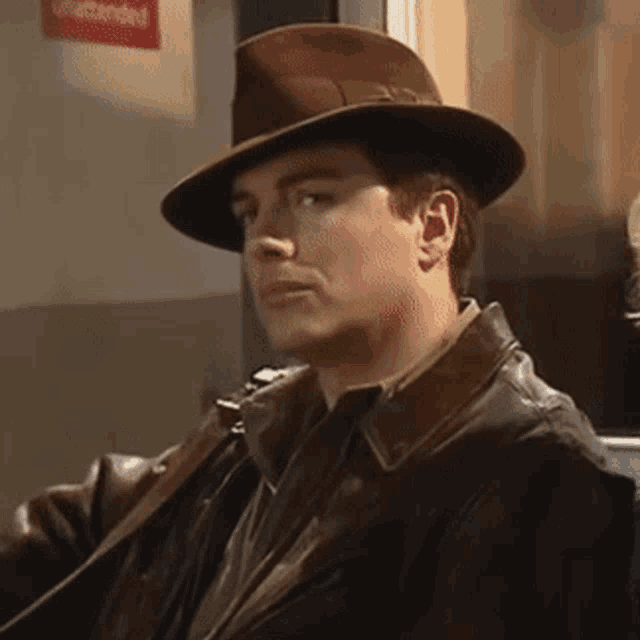 a man wearing a hat and a leather jacket is sitting in front of a sign that says unattended