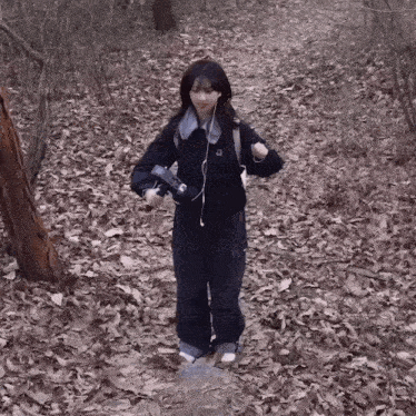a girl wearing headphones and a backpack is walking through a forest