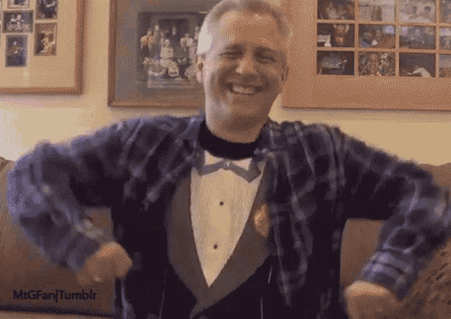 a man wearing a plaid shirt and a tuxedo is smiling and dancing