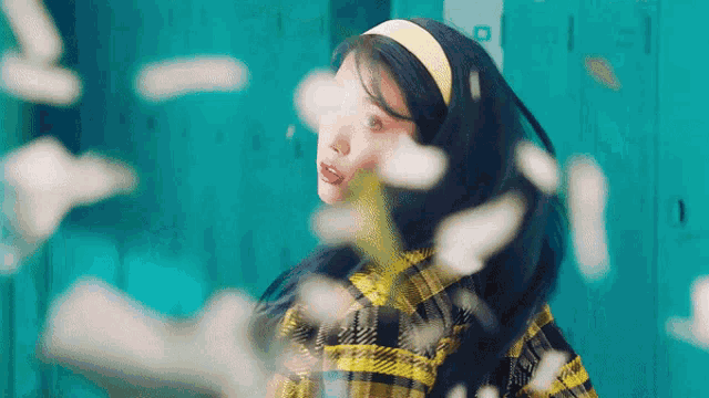 a woman in a plaid shirt is standing in front of a blue wall with flowers flying around her .