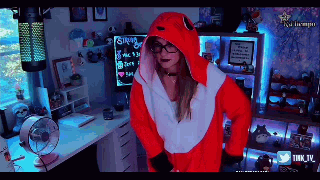 a woman in a red and white fox costume stands in front of a stream board