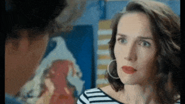 a woman with red lipstick and hoop earrings is looking at a man in front of a painting .