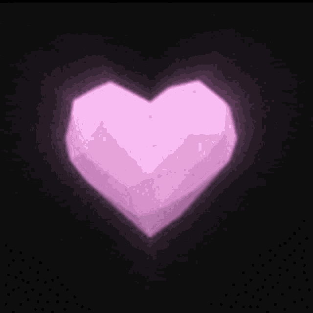 a pink heart shaped object is glowing in the dark .