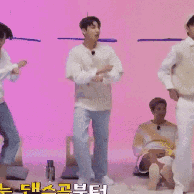 a group of young men are dancing together in front of a pink wall .