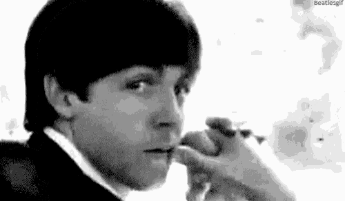 a black and white photo of a man smoking a cigarette and looking at the camera .