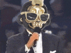 a man in a tuxedo with a skeleton mask on his face is holding a microphone