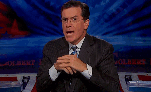 a man in a suit and tie is sitting in front of a sign that says colbert