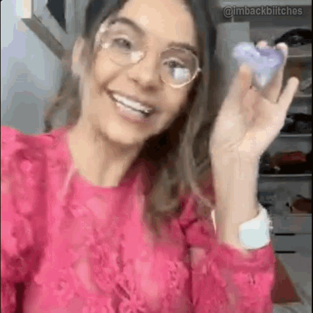 a woman wearing glasses and a pink shirt is smiling and holding a bottle of perfume .