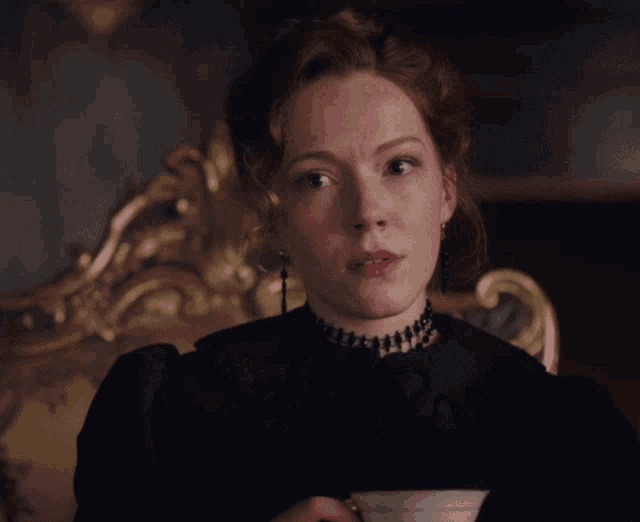 a woman wearing a choker and earrings holds a cup of coffee