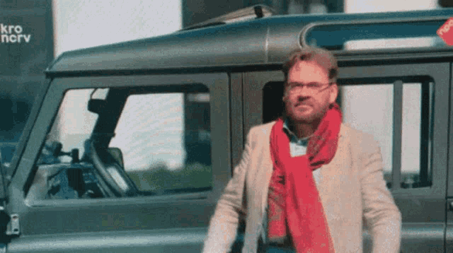 a man wearing glasses and a red scarf is standing in front of a vehicle with the letters kr on it