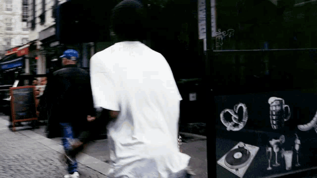 a man in a white t-shirt walks down a street