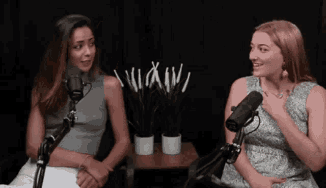 two women are sitting in front of microphones with a table with potted plants in front of them