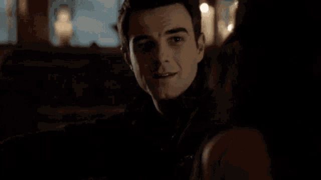 a man in a black jacket is looking at a woman in the dark .