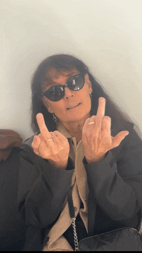 a woman wearing sunglasses and a ring giving the middle finger