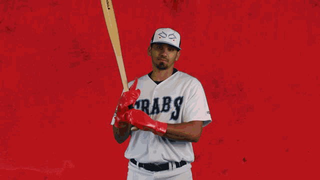 a baseball player for the crabs holds a bat in front of a red background