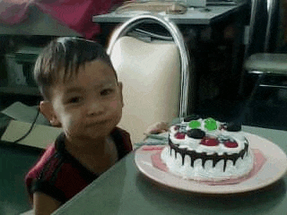 a little boy is sitting at a table next to a birthday cake .