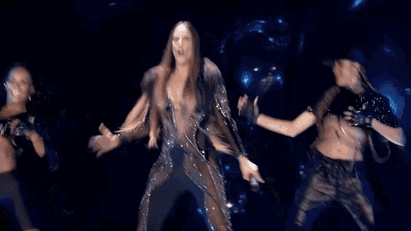 a woman in a sequined jumpsuit is dancing with two other women