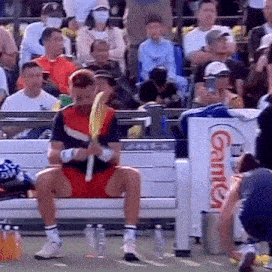 a man sits on a bench holding a tennis racquet in front of an advertisement for gameday