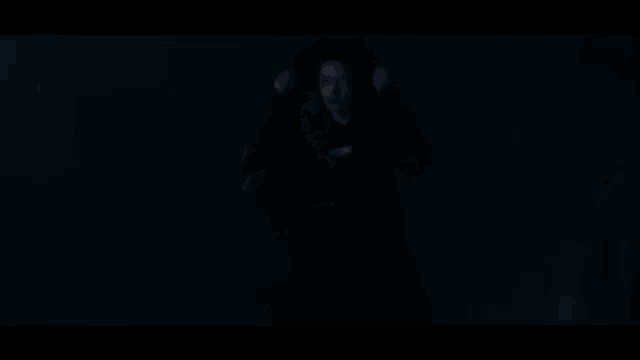 a woman in a black hoodie is standing in the dark looking at the camera .