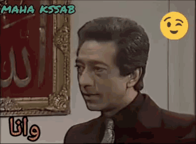 a man in a suit and tie stands in front of a framed picture with the name maha kssab on it