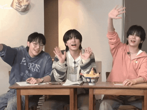 three young men sitting at a table with one wearing a sweatshirt that says paris