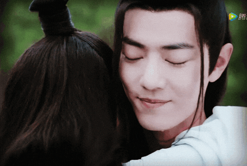 a man and a woman are hugging and the man is wearing a ponytail