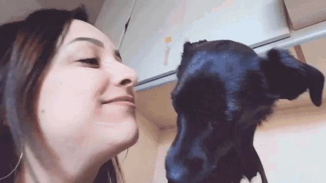 a woman is kissing a black dog on the nose .
